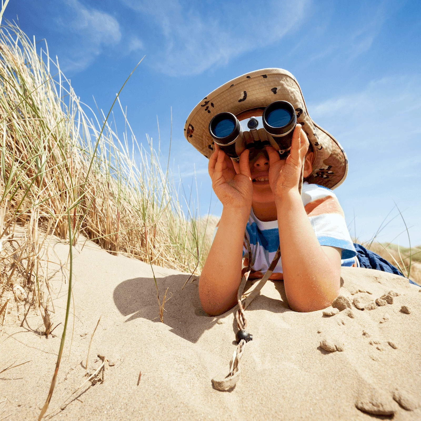 young boy in the sand looking through binoculars