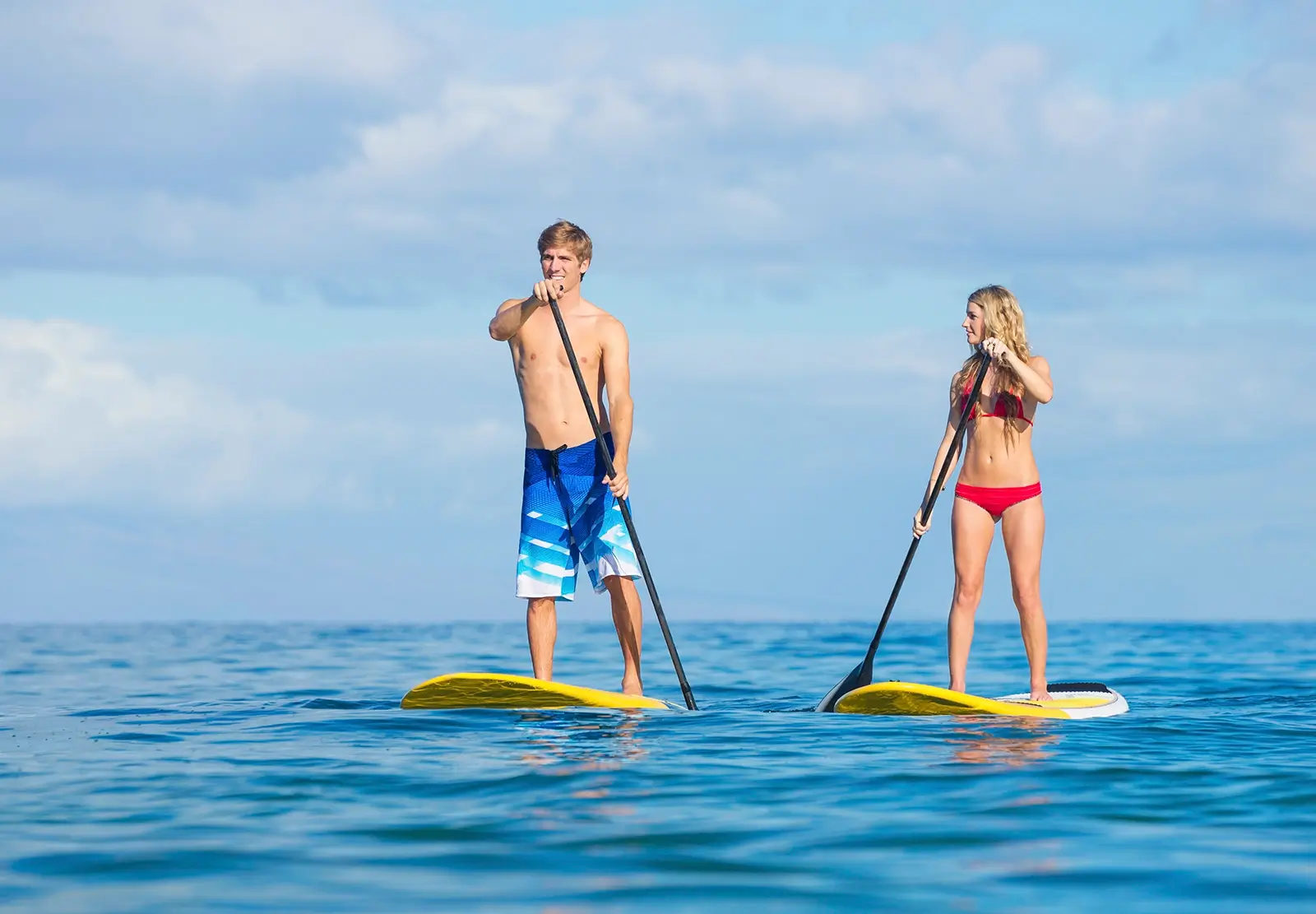attractive man and woman in bathin suits using stand up paddle boards