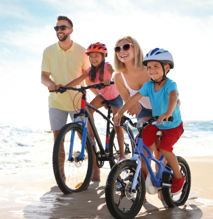 husband and wife with two young kids riding bikes on the beach